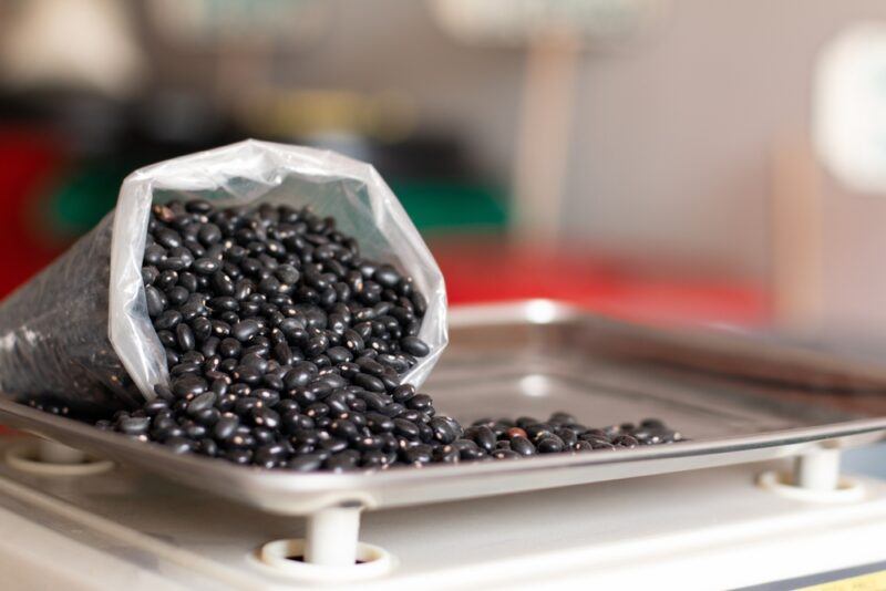 on a weighing scale is a bag of black beans with some of it spilled on to the weighing scale