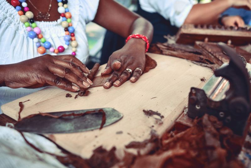 black woman hand rolling tightly wrapped dark cigar with tobacco leaves