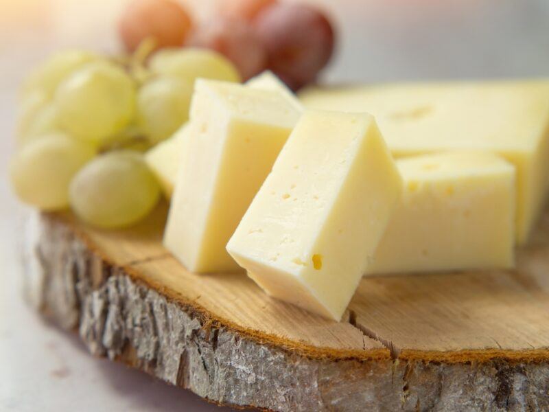 on a slab of wooden board are cubed cheese and green and red grapes behind it