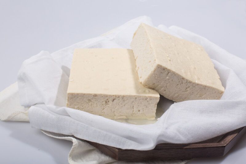 on a dark wooden tray is a white cloth with a couple of tofu blocks on it