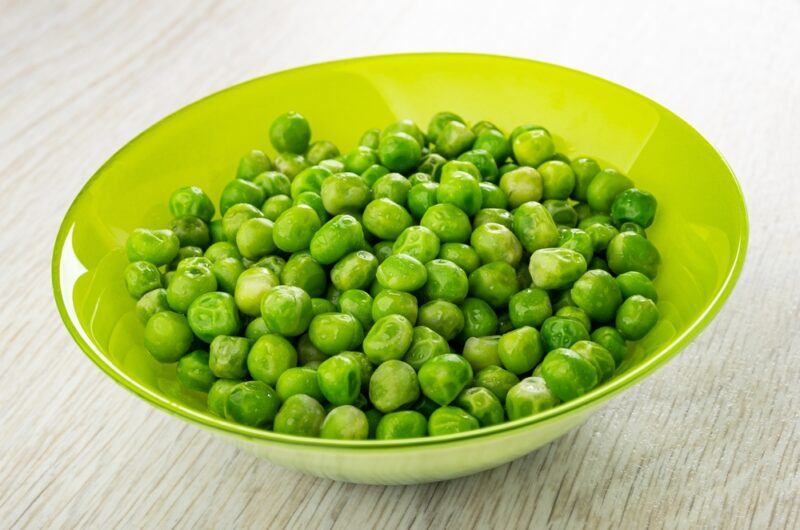 on a wooden surface is a green glass bowl full of boiled peas