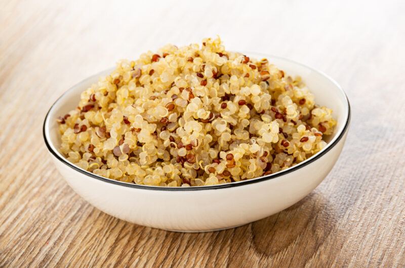 on a wooden surface is a white ceramic bowl with blue rim full of boiled quinoa