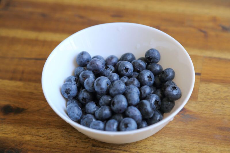 on a wooden surface is a white bowl with blueberries