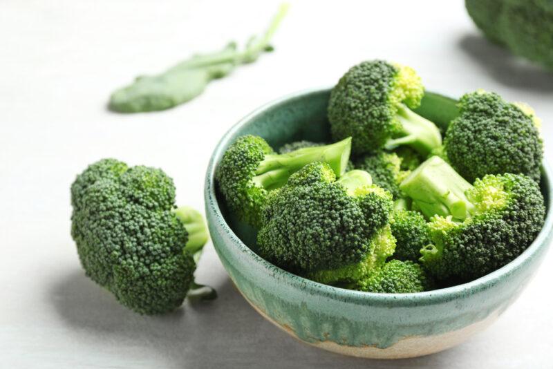 a bowl of cauliflower florets with a floret beside it and a broccoli leaf at the back