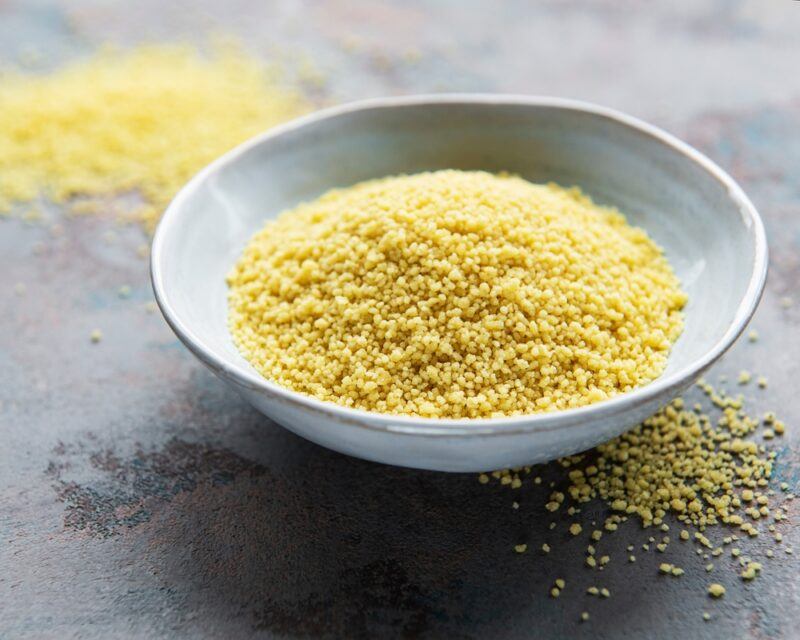 on a concrete surface is a ceramic bowl with couscous with loose couscous around it