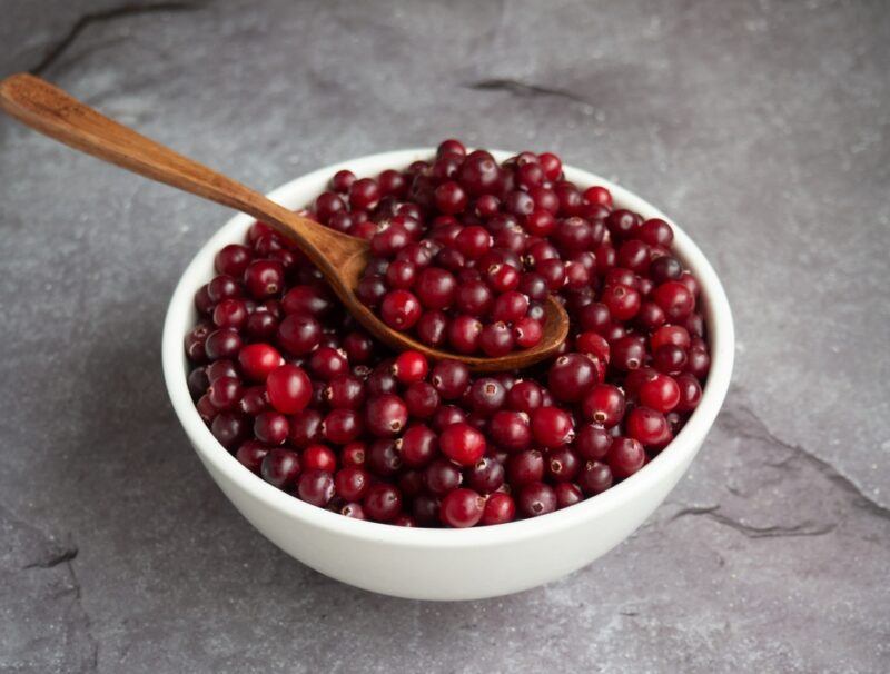 on a concrete surface is a white bowl full of fresh cranberries with a wooden spoon