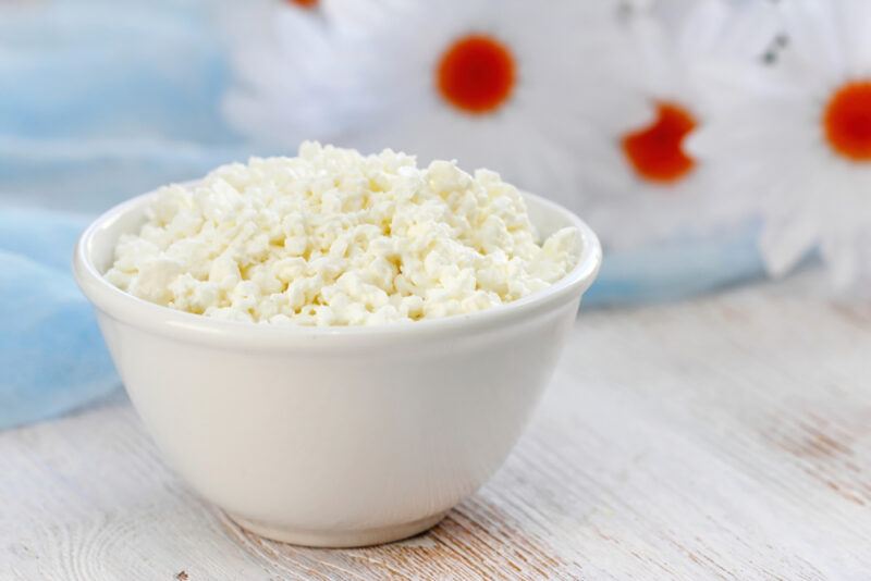 on a wooden surface is a white bowl of crumbled cottage cheese