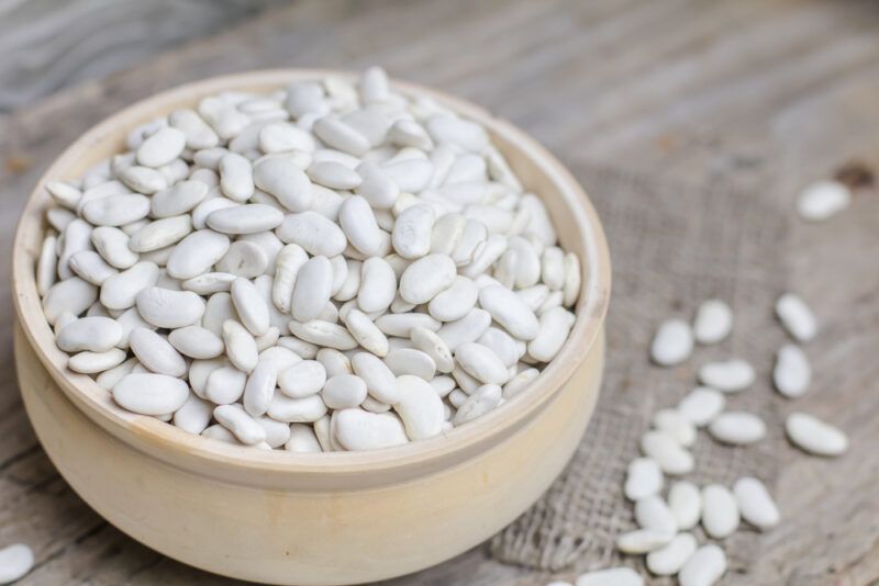 on a wooden surface is a wooden bowl full of lima beans resting on a burlap with loose lima beans beside it