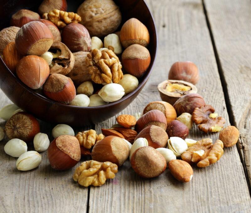 on an old wooden surface is a toppled over maroon bowl with mixed nuts, some of it were spilled over the wooden surface