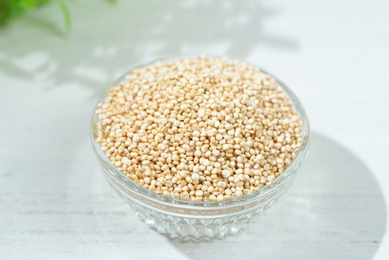 on a white wooden surface is a clear glass bowl full of quinoa