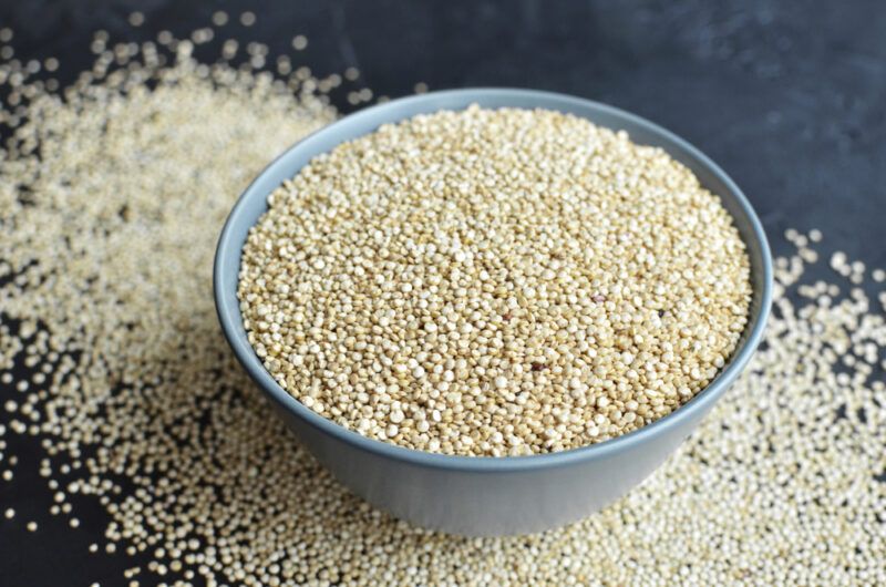 on a dark surface is a white bowl full of quinoa sitting on top of a thin spread of quinoa