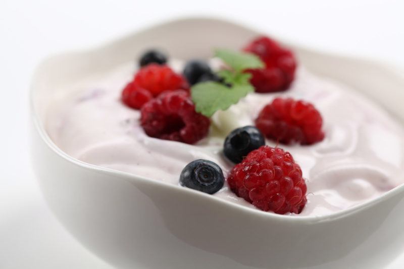 a full bowl of fresh yogurt topped with raspberries and blueberries.