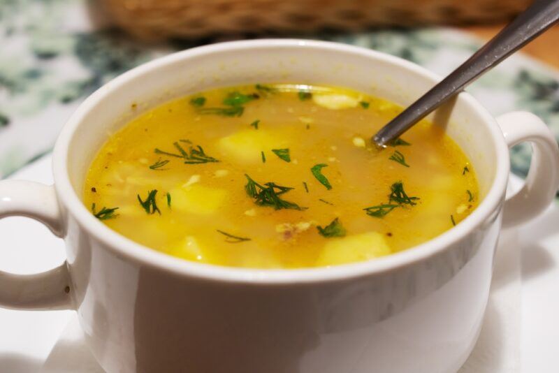 closeup image of a white bowl with yellowish broth and a silver spoon in it