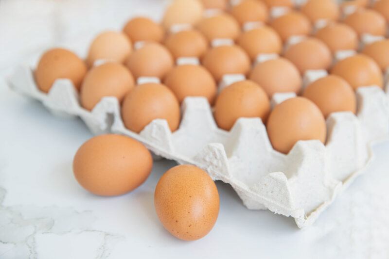 on a marble surface is a paper egg tray full of brown eggs with a couple of them laying on the marble