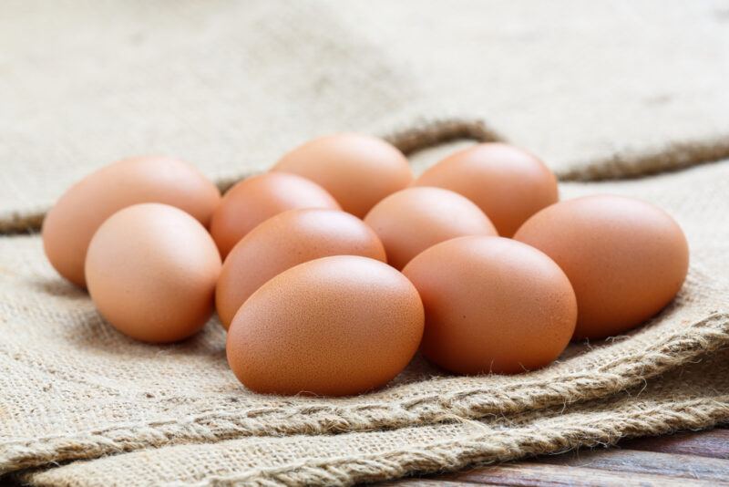 closeup image of brown eggs laid on top of a thick burlap on a wooden surface