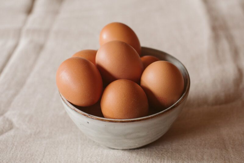 on a wooden surface is a grey ceramic bowl with brown rim full of brown eggs