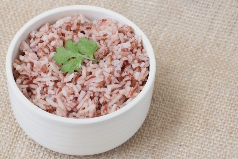 on a burlap is a white bowl full of cooked brown rice with a tiny cilantro leaf on top