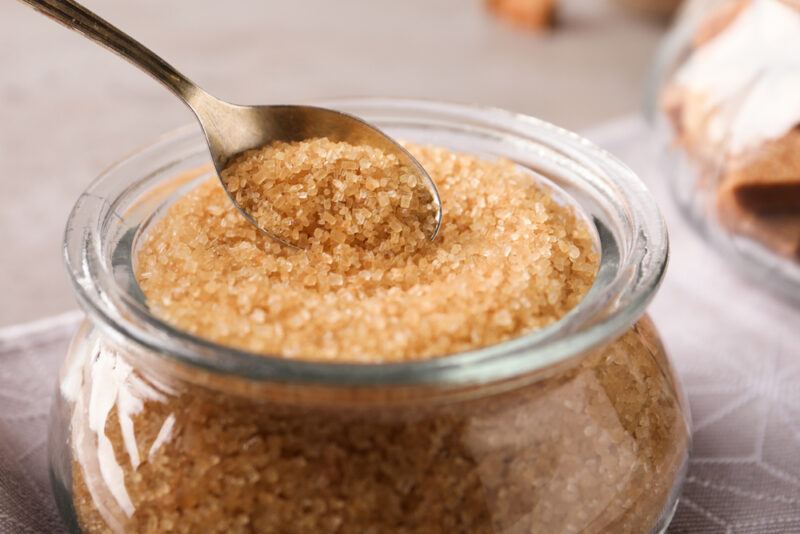 closeup image of a clear glass jar with brown sugar with a teaspoon