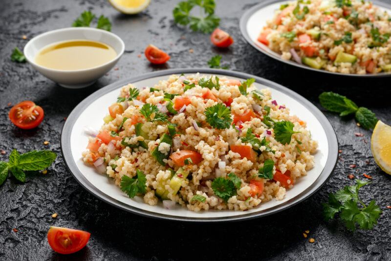 a couple of beautifully plated bulgur salad or Tabbouleh salad with loose cherry tomatoes, spices, and herbs around it along with a small dish of olive oil dressing