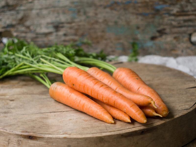 on a wooden chopping board is a bunch of fresh carrots with leaves still attached