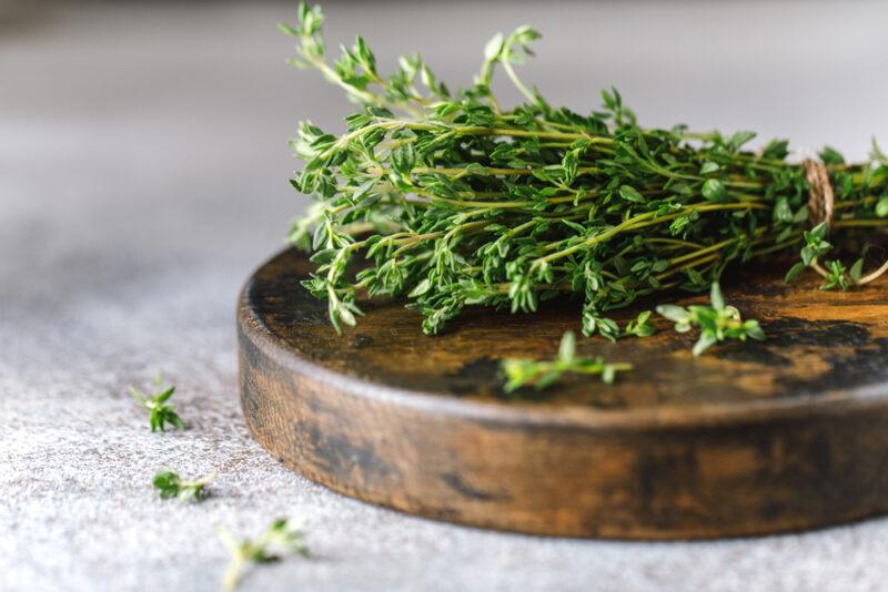 on a grey surface is an aged round wooden board with a bunch of fresh thyme held together with a brown jute