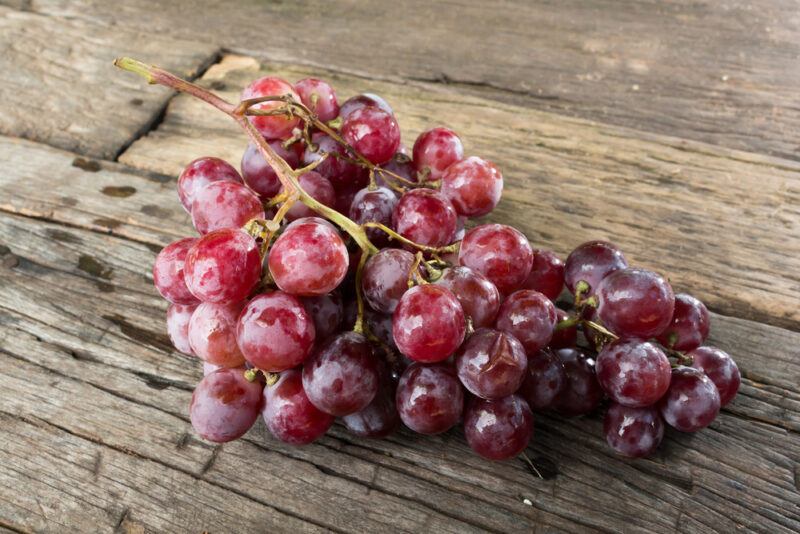 on an aged wooden surface is a bunch of red grapes