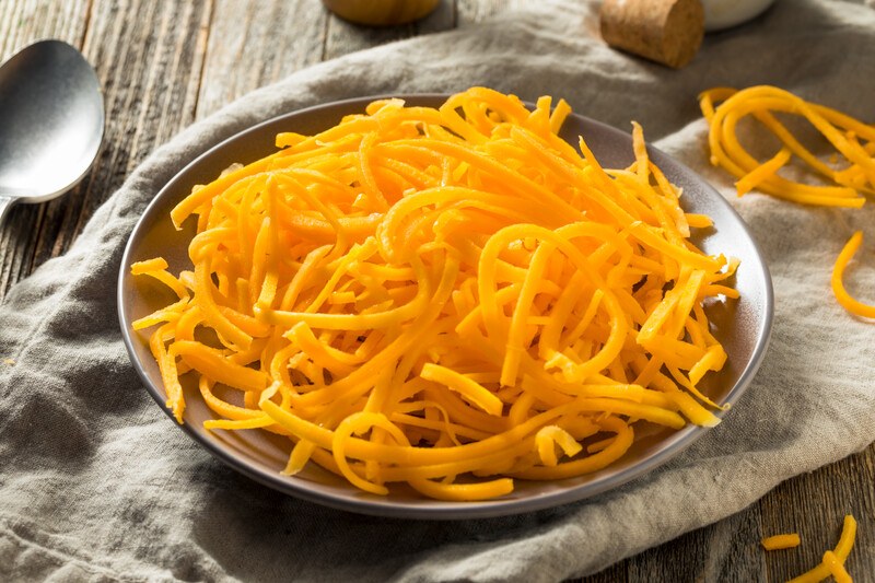 on a wooden surface is a brown dish resting on a light brown table napkin full of spiralized butternut squash