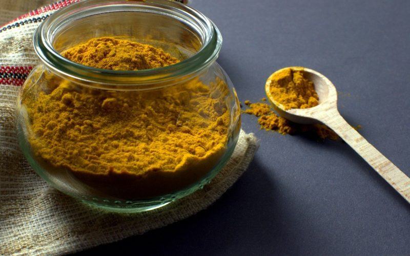 powdered turmeric in a glass jar and wooden spoon to represent where to buy fresh turmeric root online 