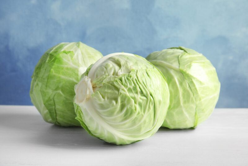 on a white surface and light blue background are three heads of cabbage