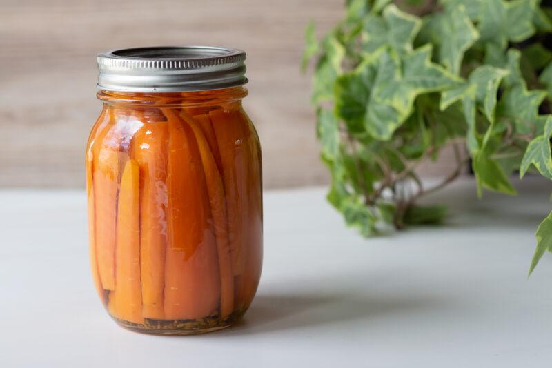 on a white surface is a mason jar of carrots with leafy greens at the back