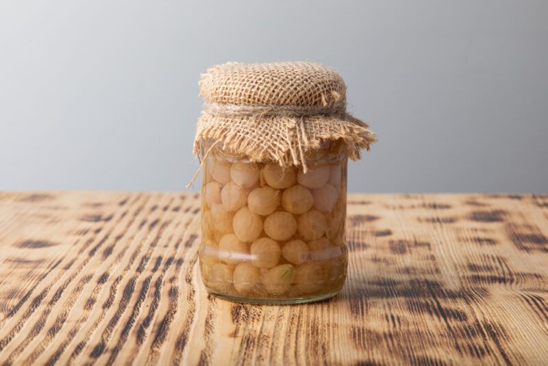 on a wooden surface is a jar of canned onions with a piece of burlap and jute covering its mouth for decor 