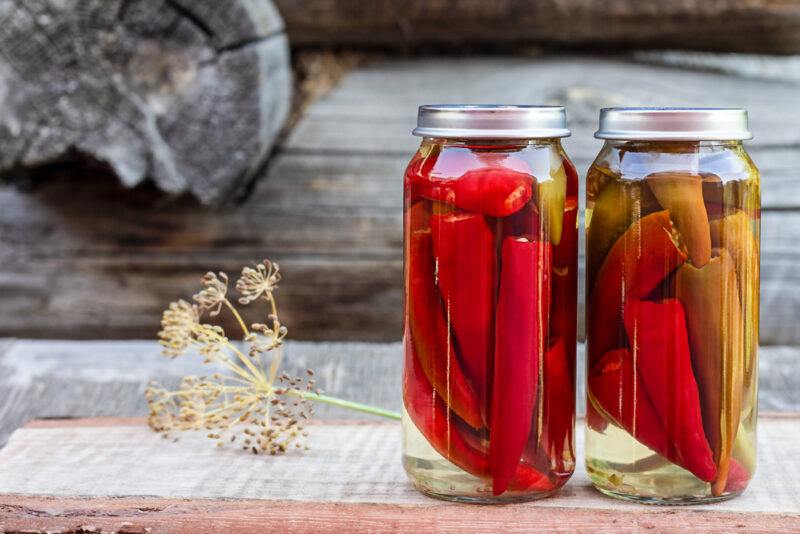 on a rustic looking wooden surface is a couple of jars with canned peppers