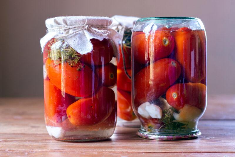 on a wooden surface are three jars with canned tomatoes, one positioned upside down