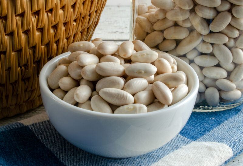 a small white bowl with cannellini beans or white kidney beans, behind it is a jar of cannellini beans and a woven container