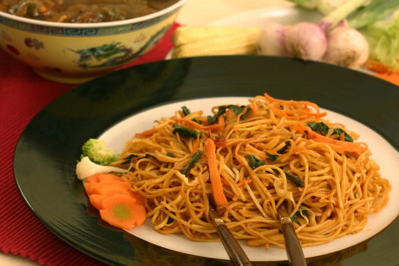 whit eplate containing sesame garlic noodles mixed with some carrots and other vegetables