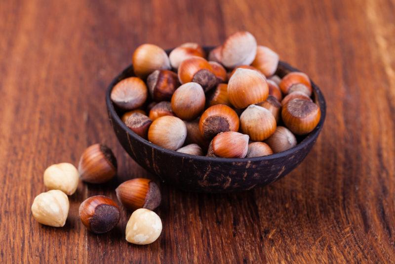a black shallow bowl filled with hazelnuts | Food For Net a wooden table with a black bowl placed on top o fit, filled with peeled and unpeeled hazelnuts