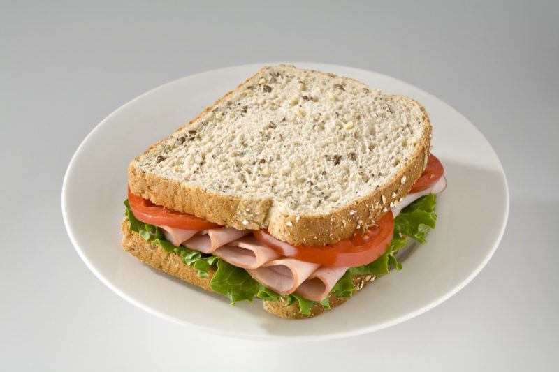 closeup shot of ham sandwich with tomatoes and lettuce on a white plate