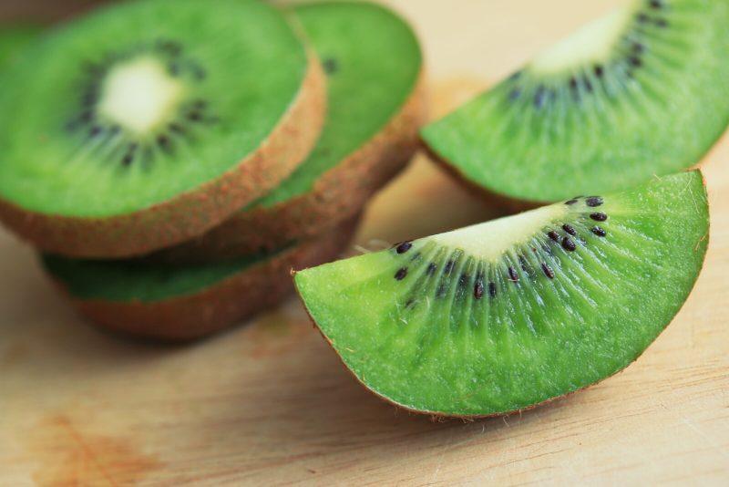 sliced and quartered kiwifruit on top of a wooden table | Food For Net closeup shot of unpeeled, sliced kiwi on a wooden table