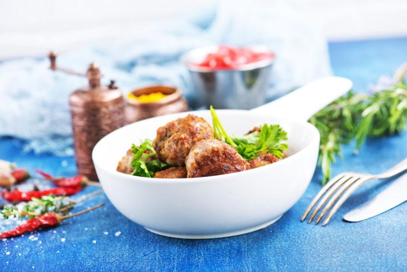 cooked honey sriracha glazed meatballs on a white bowl, topped by some greens