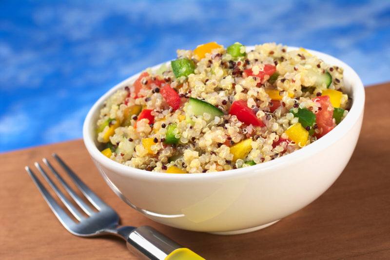 white bowl containing cooked quinoa mized with cucumbers, tomatoes and salad dressing