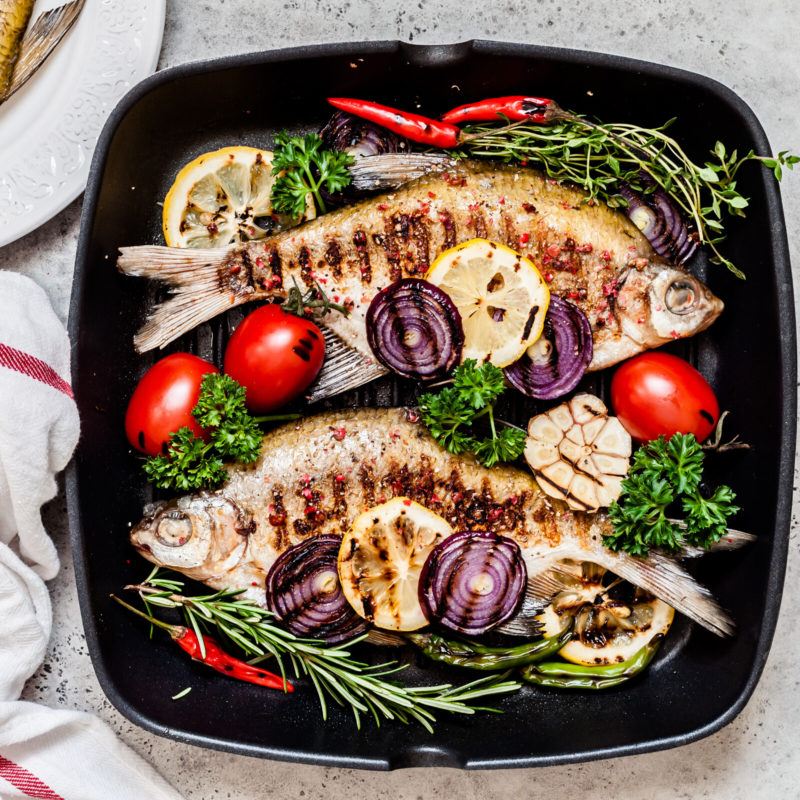 pan fried fish with red tomatoes, onion, red peppers and herbs resting in hot skillet removed from its base