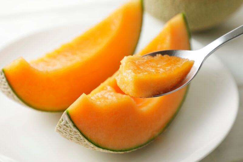 on a white plate with a couple of slices of cantaloupe and a silver spoon with a piece of cantaloupe