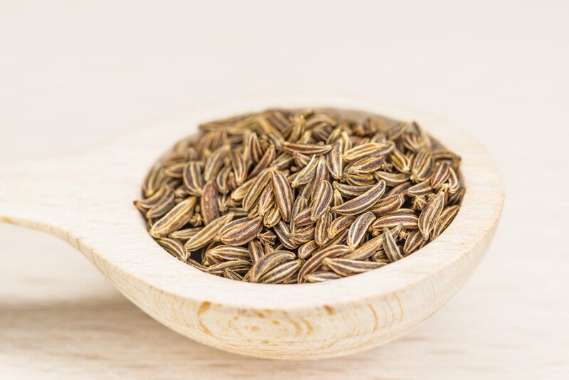 on a wooden surface is a closeup image of a wooden ladle full of caraway seeds