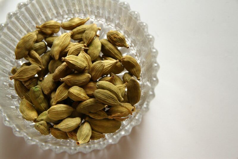 on a white surface is a top view image of a glass bowl with cardamom pods