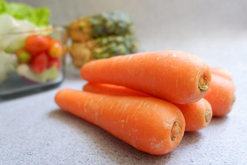 on a concrete surface is a pile of whole carrots with other veggies at the back