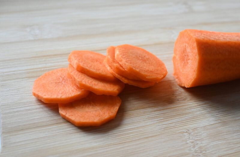 closeup image of partially sliced carrots on a wooden chopping board