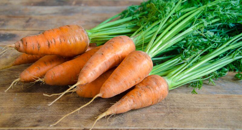 on a wooden surface is a bunch of fresh carrots with green tops still attached