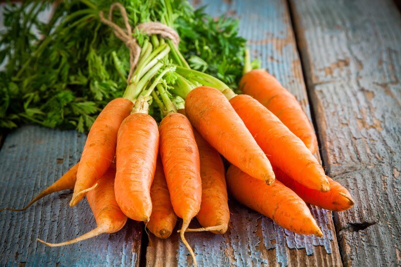 on a rustic looking wooden surface is a bunch of carrots with leaves still attached