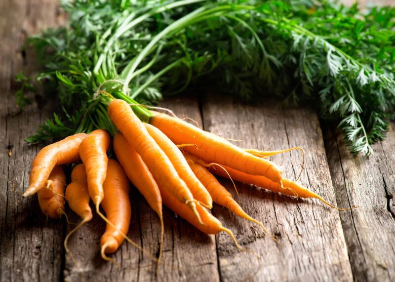 on a rustic looking wooden surface is a bunch of baby carrots with leaves still attached