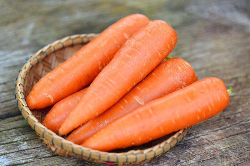 on a rustic looking wooden surface is a basket full of whole carrots